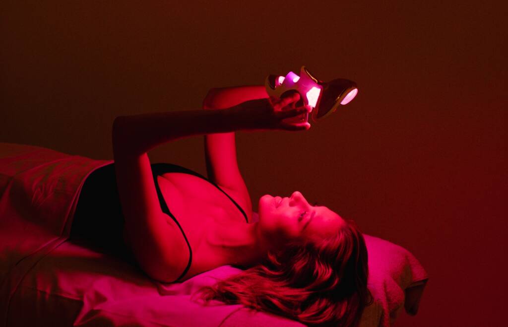 Woman lying on a spa bed applying an LED face mask at RoseBar